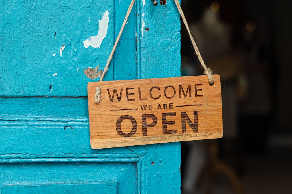 A rustic wooden 'Welcome We Are Open' sign hanging on a vibrant blue door.