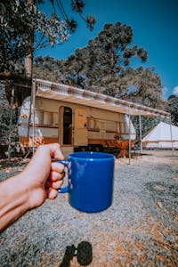 Blue mug held in a pine forest campsite with caravan in Fracalanza, Brazil.